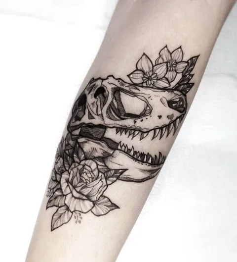 Crânio de dinossauro com rosas e flores, em traço preto e sombra pontilhada, no antebraço