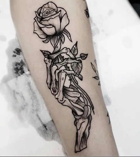 Mão de esqueleto segurando uma rosa, em contorno preto grosso, no antebraço