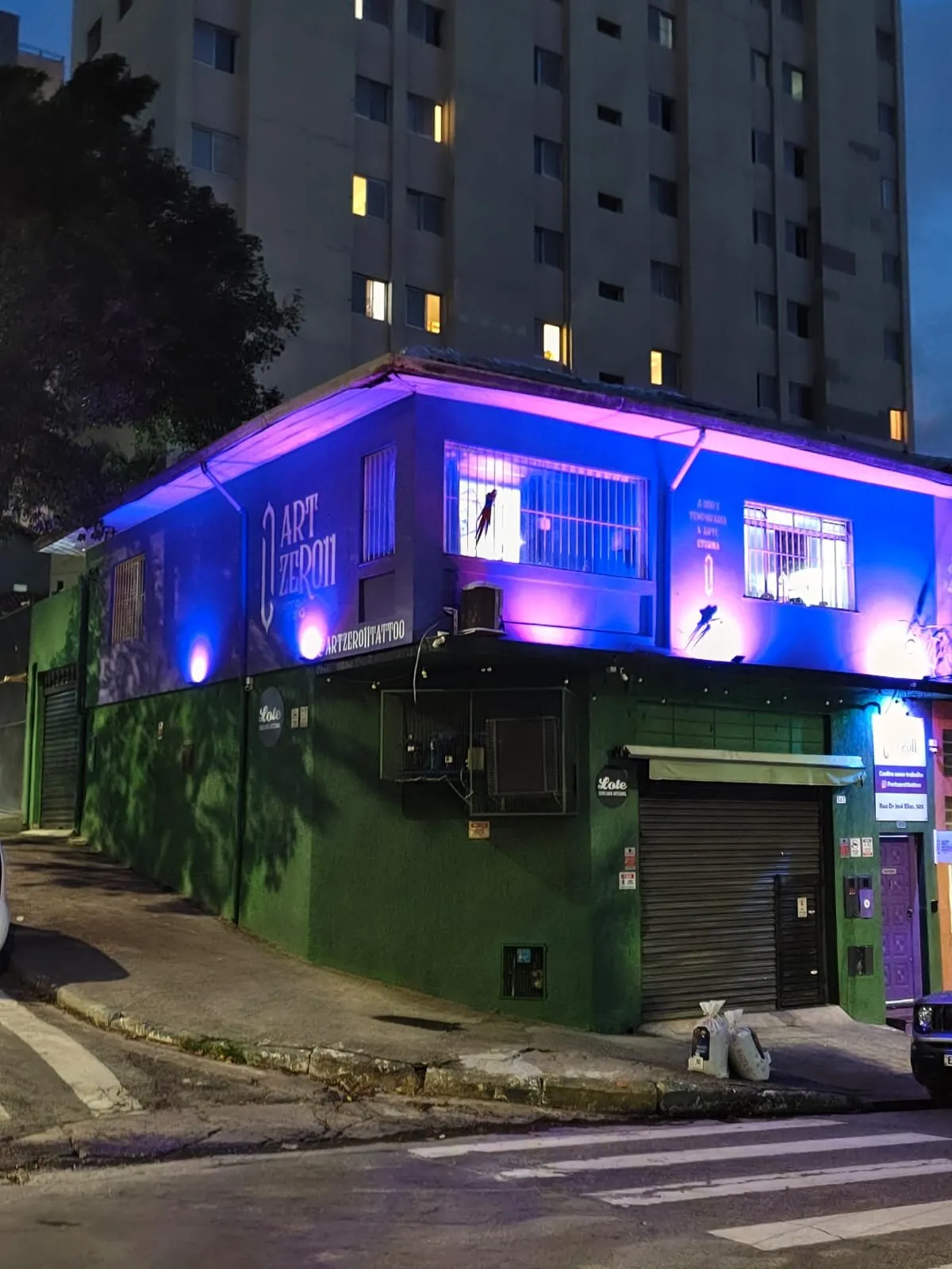 Fachada do ArtZero11 Tattoo Studio à noite, iluminada de roxo, na esquina da Rua Dr. José Elias, no Alto da Lapa
