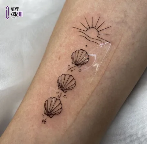 Sol nascendo sobre o mar e três conchas em sequência, em traço fino no antebraço