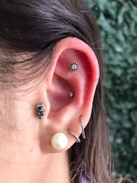Composição na orelha: piercings na cartilagem de cima e do meio, e argolas e uma pérola no lóbulo