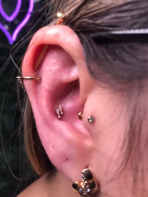 Piercing industrial, uma barra atravessando a parte de cima da orelha, com piercing no tragus e no meio da orelha