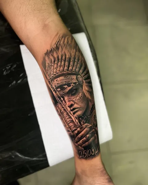 Mulher indígena com cocar de penas, em realismo preto e cinza, no antebraço